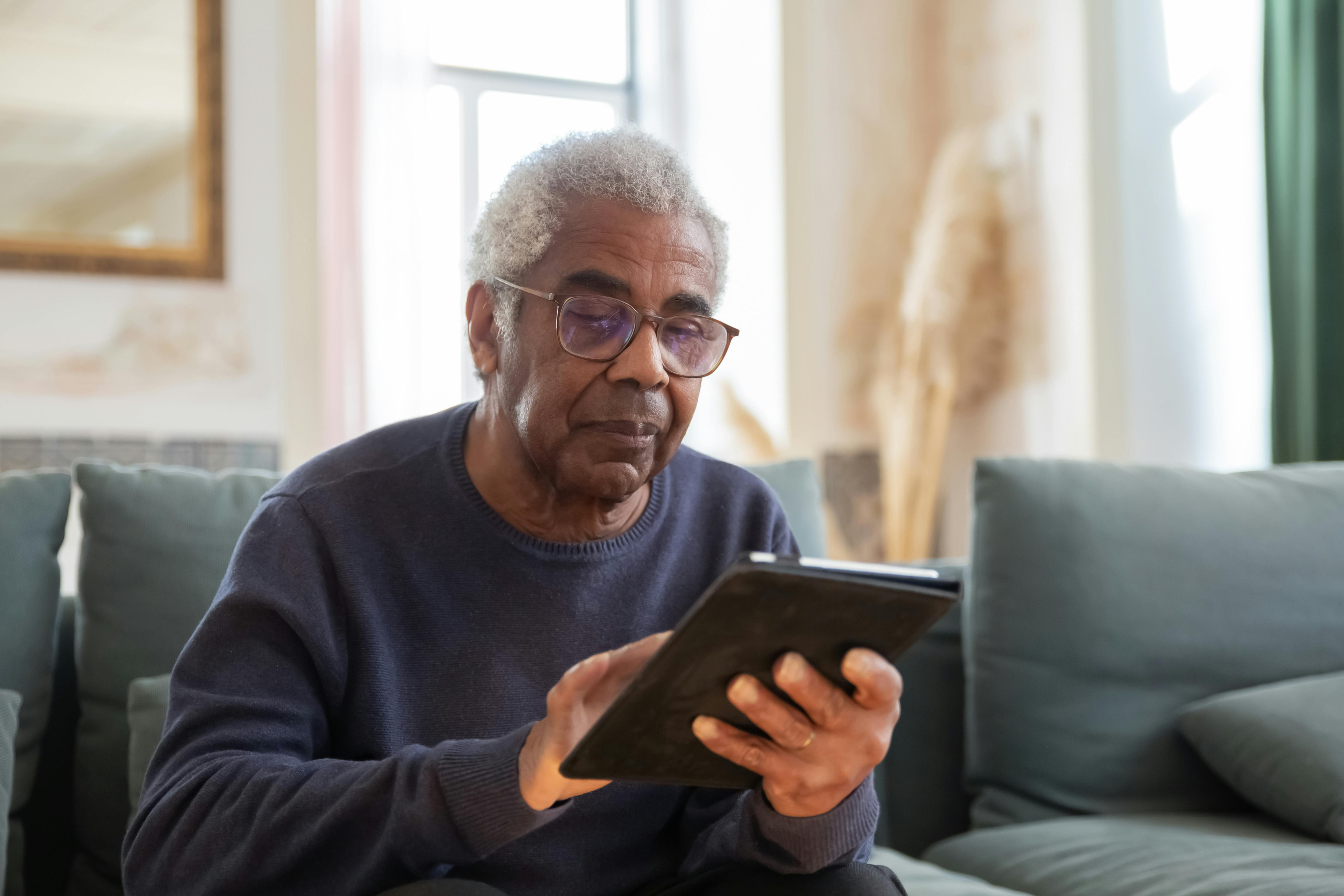 Älterer Mann übt entspannt zu Hause auf dem Sofa mit einem Tablet